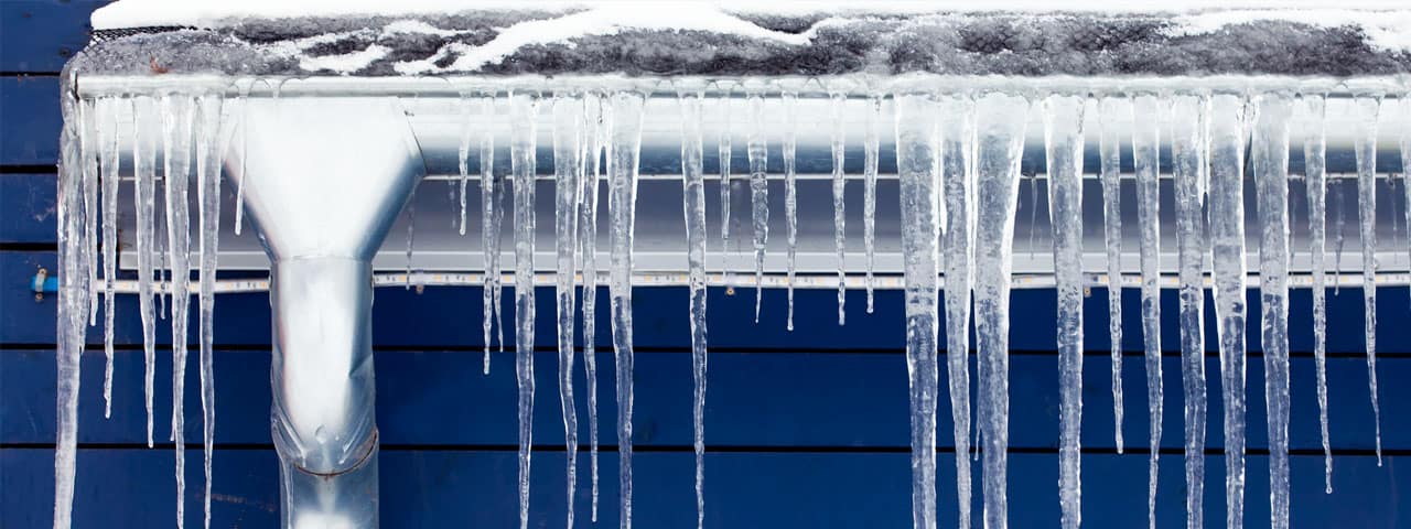 Ice dam and icicles forming at the edge of a snow-covered roof