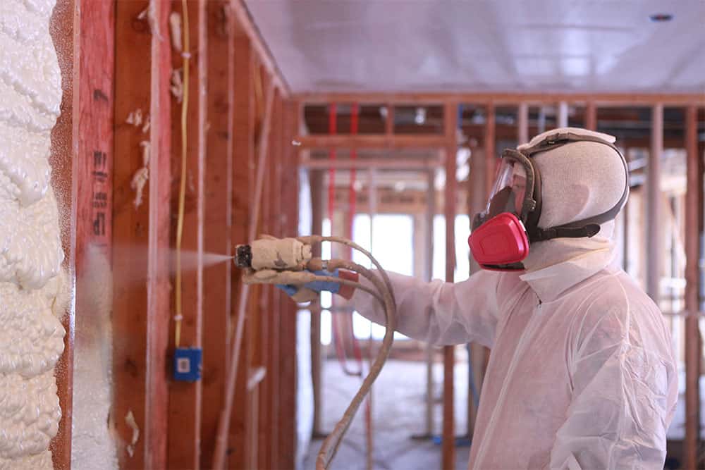 Certified spray foam applicator in full respirator gear spraying foam insulation